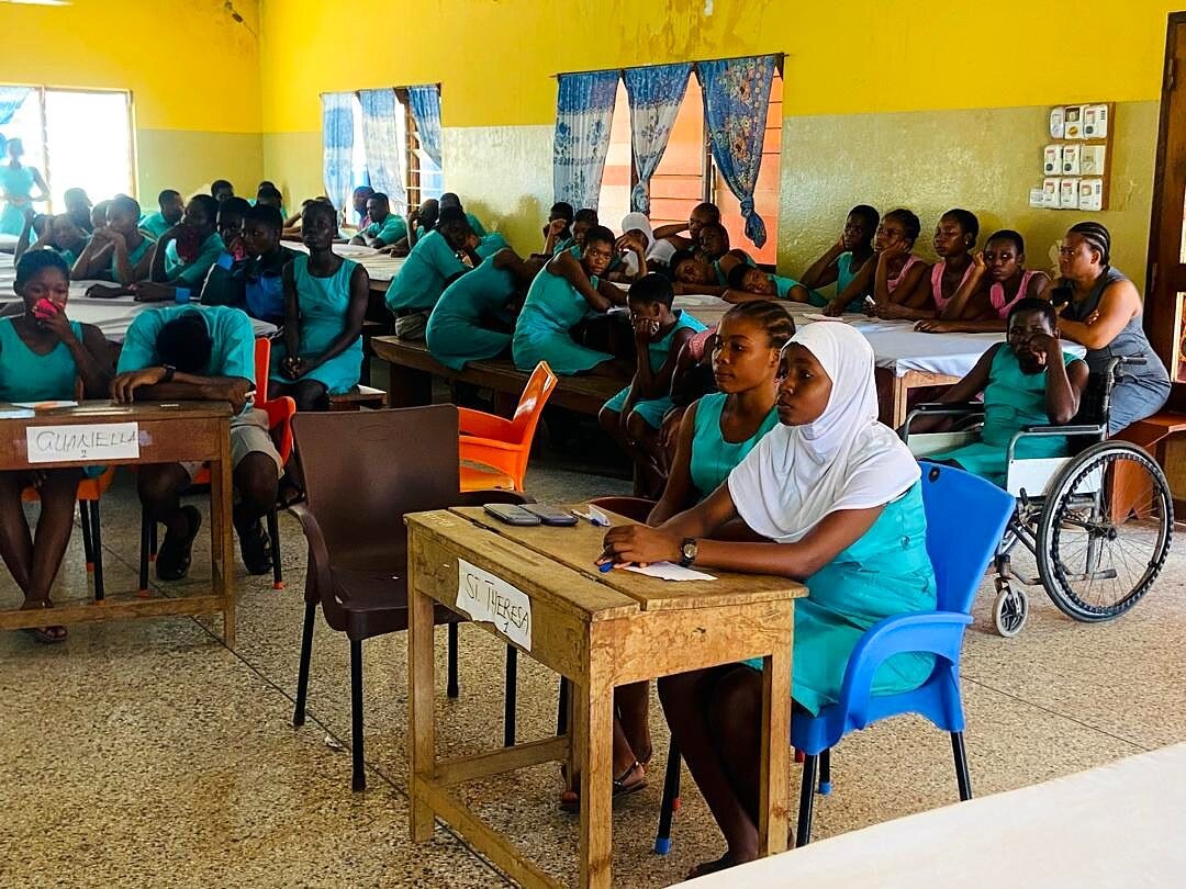 Aula del centro affollata di studenti in divisa; sul fondo una carrozzina.